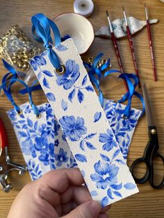 a person holding a piece of paper with blue flowers on it next to scissors and other crafting supplies