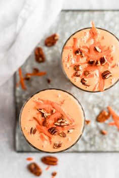 two glasses filled with carrot smoothie topped with pecans