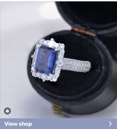 an engagement ring with a large blue stone surrounded by small white diamonds in a black velvet box