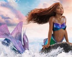 a beautiful young woman sitting on top of a rock next to a purple mermaid tail