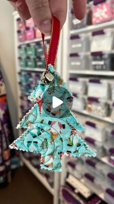 a person holding up a christmas tree ornament in a store with other items on the shelves