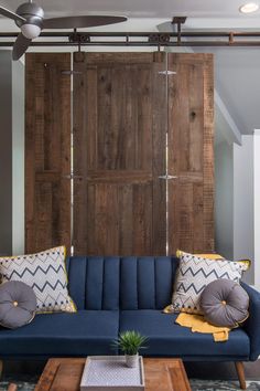 a blue couch sitting in front of a wooden wall with two pillows on top of it