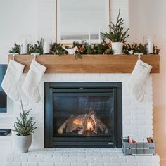 a fireplace decorated for christmas with stockings and potted plants on the mantel above it