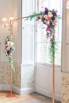 an arch decorated with flowers and greenery stands in the corner of a room next to a window