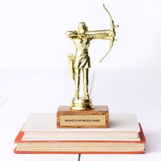 a golden statue holding a bow and arrow on top of two bookends that are stacked next to each other