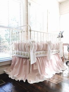 a white crib with pink ruffled bedding in front of a large window