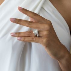 a woman's hand with a diamond ring on her left thumb, wearing a white dress