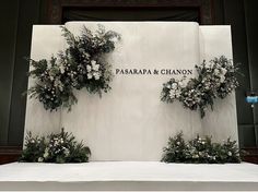 flowers and greenery are arranged on the side of a white wall with words that read pasarapa & chanon