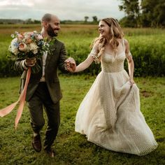 a bride and groom holding hands walking through the grass