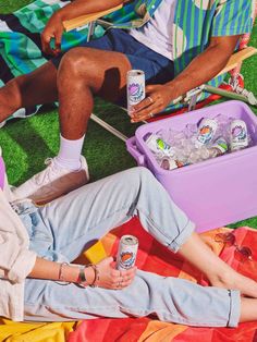 two people are sitting on the grass with drinks in their hands and one person is holding a drink