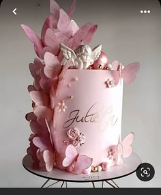 a pink cake decorated with flowers and butterflies on a metal stand in front of a white wall