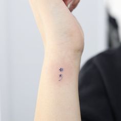 a woman's arm with a small tattoo on her left wrist and stars on it