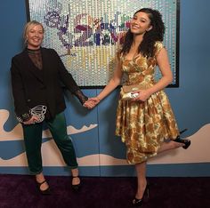 two women standing next to each other holding hands in front of a painting on the wall