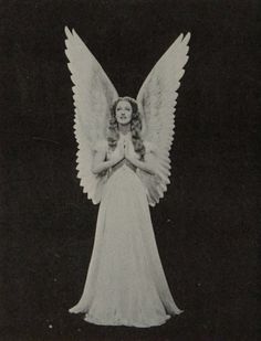 an old black and white photo of a woman dressed as an angel with her hands folded in prayer