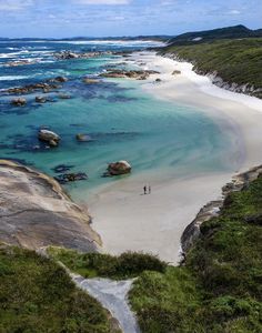 two people are standing on the beach looking out at the water and rocks in the ocean