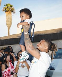 a man holding up a small child in front of a group of people with tattoos on their arms