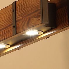 three lights that are on the side of a wooden beam in a room with white walls