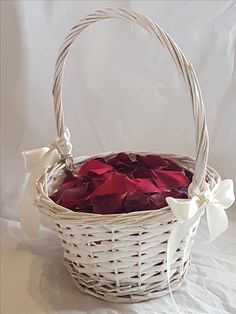 a white basket filled with red roses on top of a bed covered in white sheets