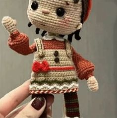 a crocheted doll is being held up by someone's hand and wearing a red hat