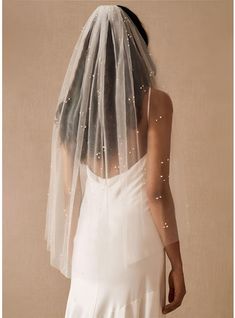 the back of a woman wearing a wedding veil with pearls on it's head