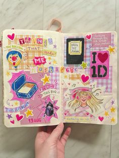 a hand holding an open notebook with stickers on the pages and pictures in it