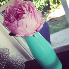 a pink flower in a green vase on a window sill next to a blue pillow