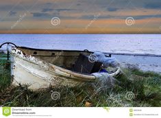 an old boat sitting on the grass by the ocean at sunset or dawn with clouds in the background