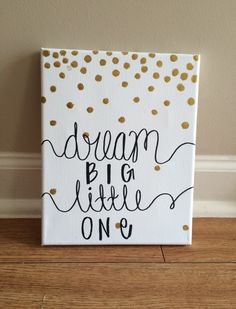 a white canvas with gold dots and the words dream big little one on it in black ink