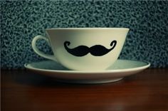 a coffee cup with a mustache painted on the side sitting on a saucer in front of a wall