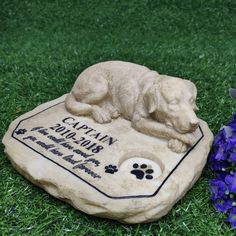 a dog memorial is placed on the grass next to purple flowers and blue hydrant