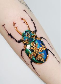 a beetle tattoo on the arm with gold and blue details around it's legs