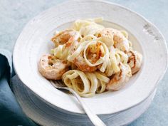 a white bowl filled with pasta and shrimp on top of a blue table cloth next to a fork