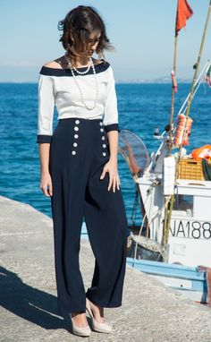 "If you live on an island, going on a boat is like riding a biking. This is the reason why we love the sailor's style that we've adapted for this elegant outfit made up of a white blouse with dark blue contrasting trim and zipper on the back, coupled with blue high waist trousers with a soft cut. Suitable for an evening at the sea, on a yacht or in the city (dreaming of the sea this outfit will accompany you from spring to autumn, so you can step out in great style. We think this dress would loo Trousers Summer Outfit, Sailor Pants Outfit, Sailor Outfit For Women, Nautical Clothing, Sailor Blouse, Blue And White Outfits, Elegant Trousers, Sailor Outfit, Outfit Navy