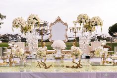 a table topped with lots of vases filled with white flowers and candles next to a mirror