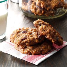 three oatmeal cookies sitting on top of a napkin next to a glass of milk