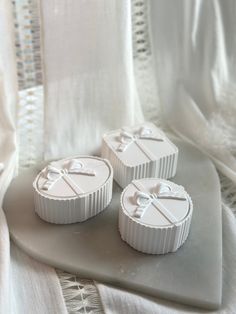 three small white boxes with bows on them sitting on a tableclothed surface next to a curtain