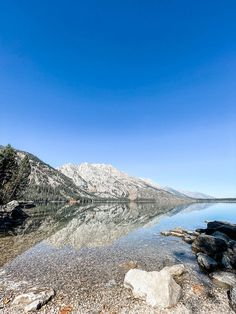 a mountain range is reflected in the still water of a lake on a sunny day