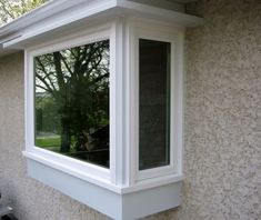 a white window on the side of a house with trees in the backgroud