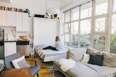 a woman sitting on top of a couch in a living room next to a window