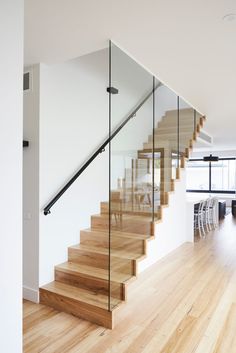 a wooden staircase with glass railing and handrails in a modern home, looking into the dining room