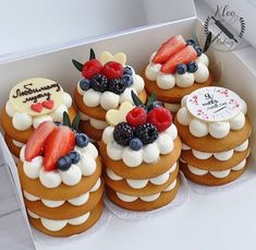 a box filled with lots of cakes covered in frosting and fruit on top of each other