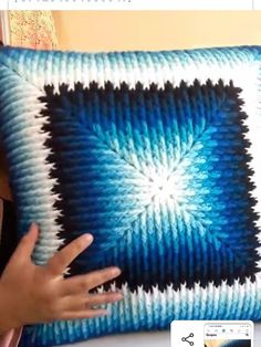 a person holding up a blue and white knitted pillow with an interesting design on it