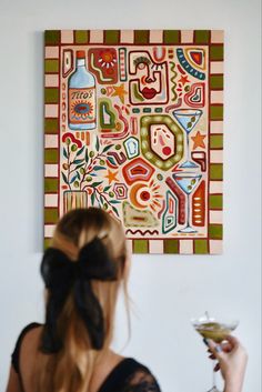 a woman holding a martini glass in front of a painting on the wall behind her