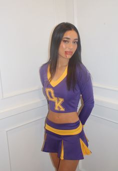 a woman in a purple and yellow cheerleader outfit posing for the camera with her hands on her hips