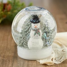 a snow globe with a snowman inside on a wooden table next to a lace doily