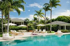 an outdoor pool with lounge chairs and umbrellas next to the swimming pool surrounded by palm trees