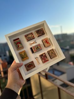 a person holding up a box filled with different types of magnets on top of a balcony