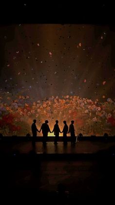 silhouettes of people holding hands in front of a large screen with flowers on it