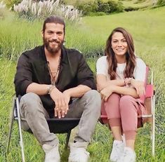 a man and woman sitting in chairs on the grass with their arms crossed, smiling at the camera