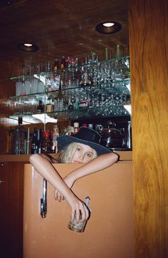 a woman wearing a cowboy hat leaning on a brown suitcase in front of a bar